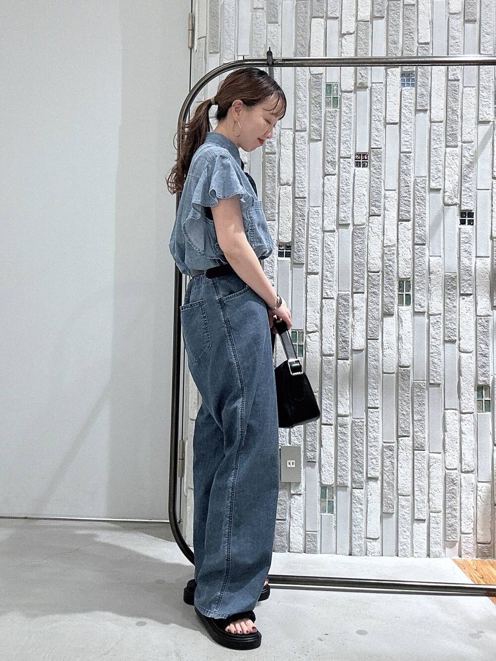 ブルー系のデニムパンツ、ブラック系のサンダル、ブラック系のショルダーバッグを着用したレディースの春コーディネートの3枚目の写真