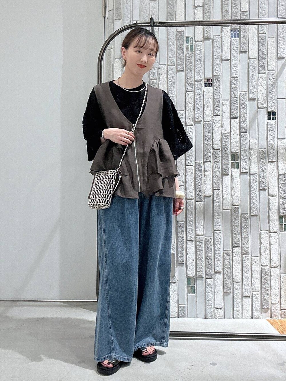 ブルー系のデニムパンツ、ブラック系のサンダル、シルバー系のショルダーバッグを着用したレディースの夏コーディネートの2枚目の写真