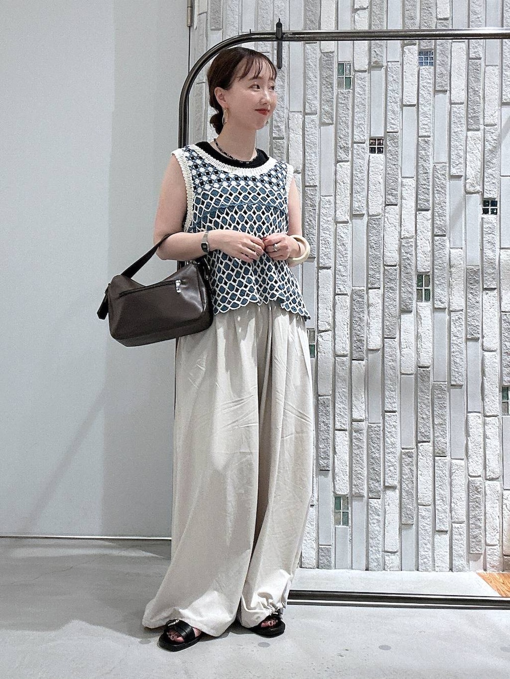 ブラウン系のショルダーバッグ、ブルー系のベスト、ブラック系のサンダルを着用したレディースの夏コーディネートの2枚目の写真