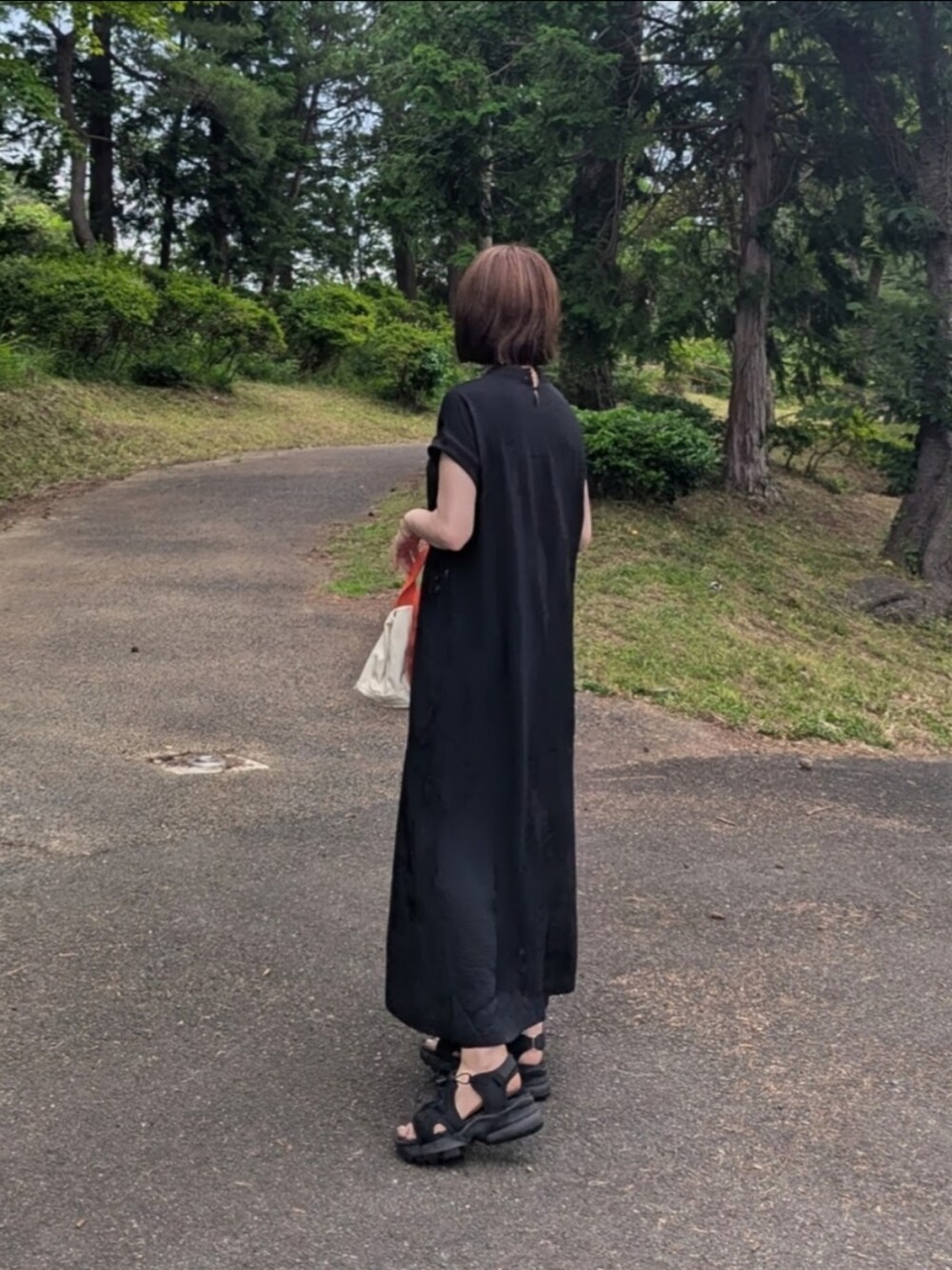 ブラック系のワンピース、オレンジ系のトートバッグ、ブラック系のサンダルを着用したレディースの夏コーディネートの3枚目の写真
