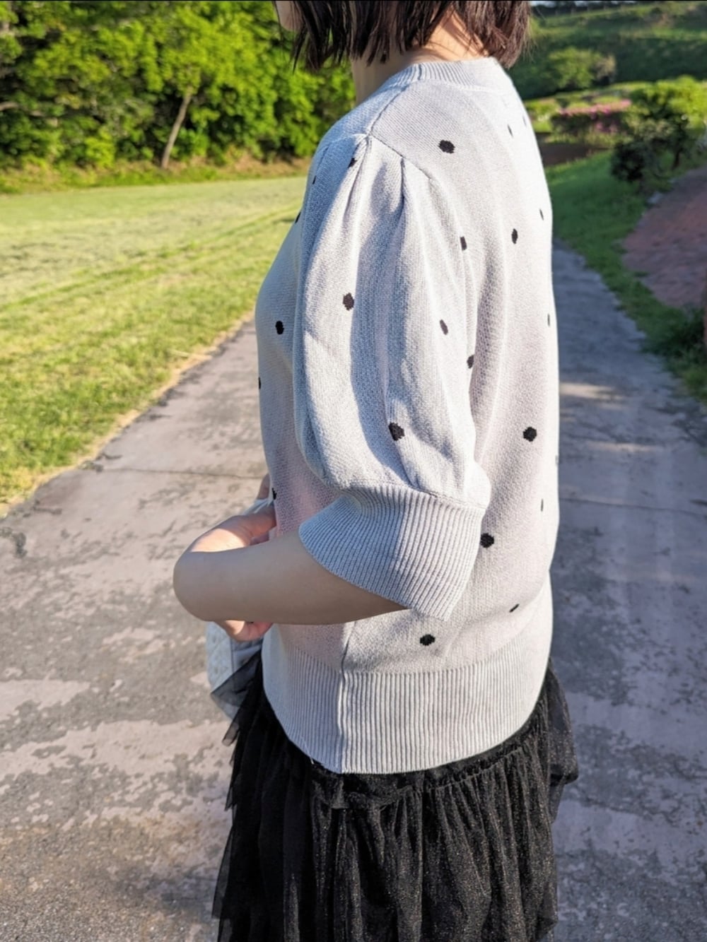 グレー系のニット/セーター、ブラック系のスカート、ホワイト系のハンドバッグを着用したレディースの春コーディネートの3枚目の写真