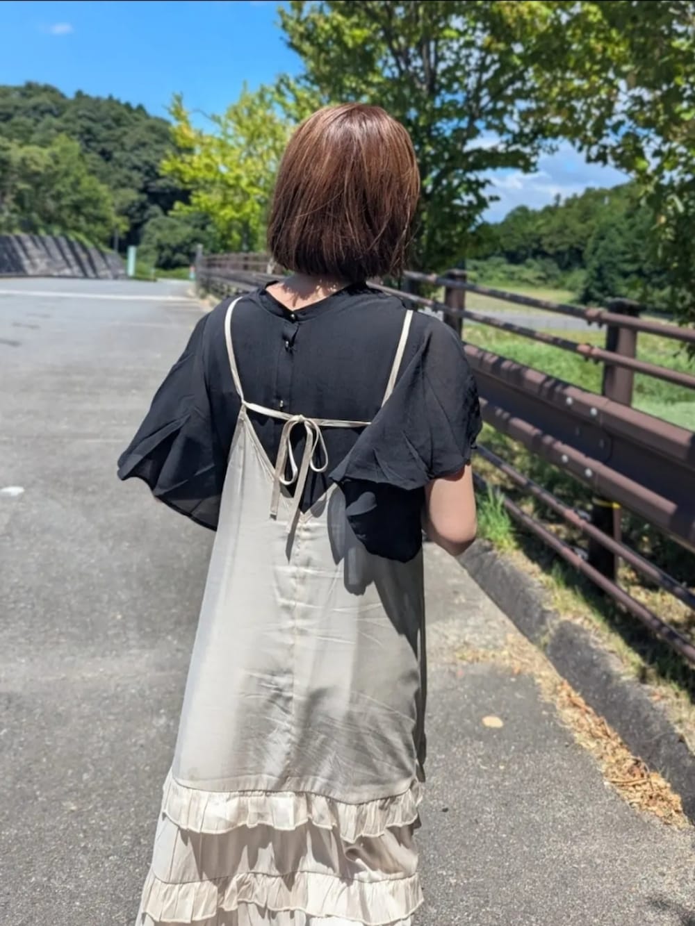 ブラック系のシャツ/ブラウス、シルバー系のサンダル、ベージュ系のショルダーバッグを着用したレディースの夏コーディネートの2枚目の写真