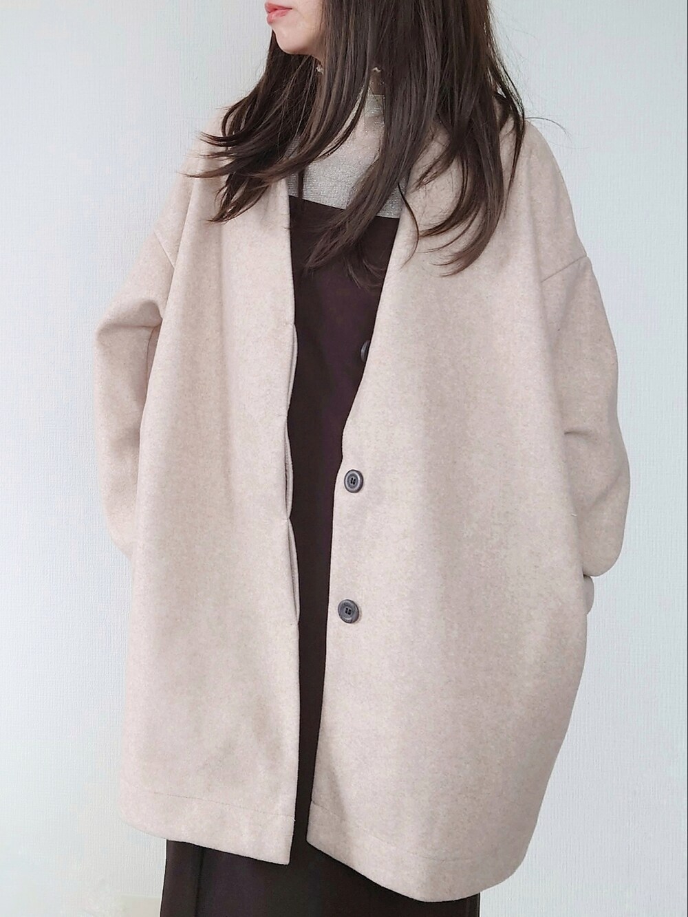 ベージュ系のノーカラーコート、ブラウン系のクラッチバッグ、ブラウン系のワンピースを着用したレディースの秋コーディネートの2枚目の写真