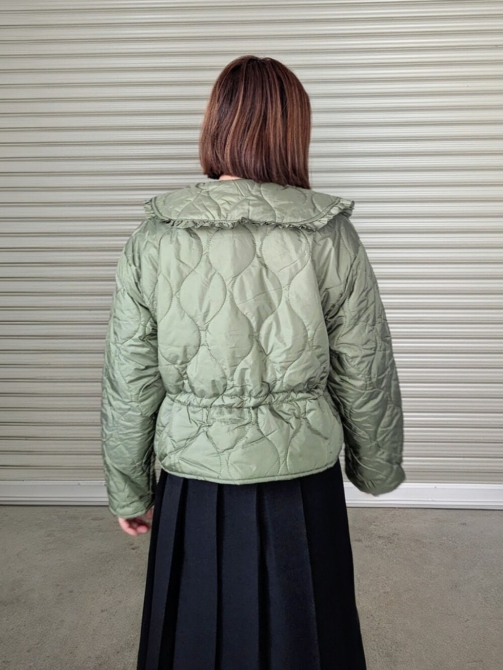 グリーン系のダウンジャケット/コート、ホワイト系のニット/セーター、ブラック系のブーツを着用したレディースの秋コーディネートの2枚目の写真