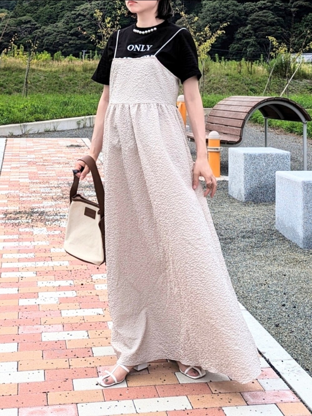 ベージュ系のワンピース、ブラック系のTシャツ/カットソー、ブラウン系のハンドバッグを着用したレディースの夏コーディネートの2枚目の写真