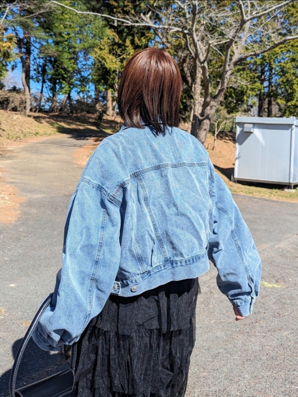 ブルー系のデニムジャケット、ブラック系のスカートを着用したレディースの春コーディネートの2枚目の写真