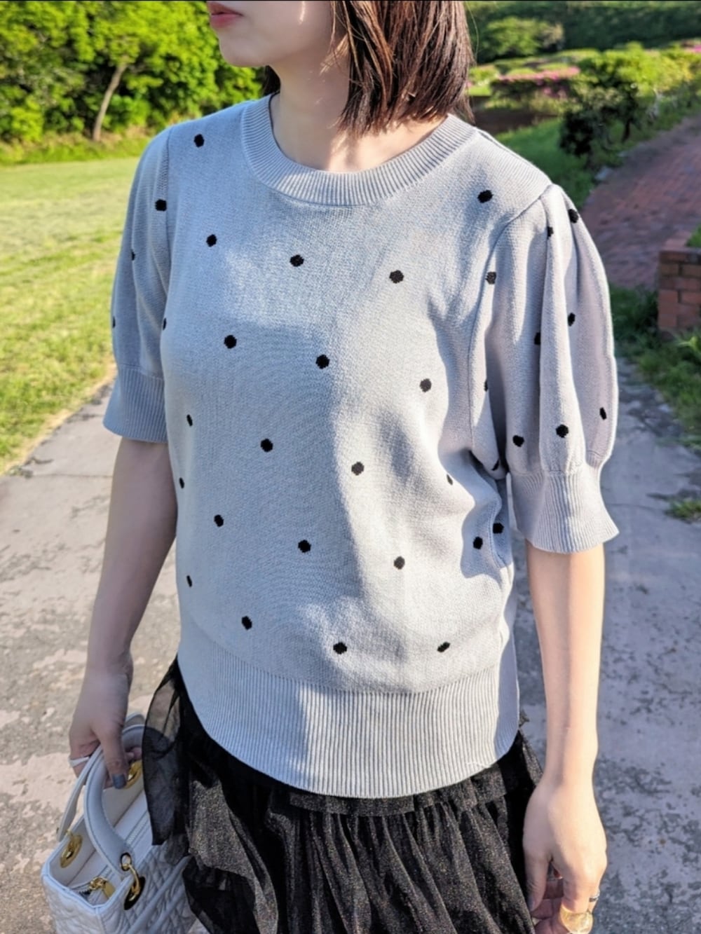 グレー系のニット/セーター、ブラック系のスカート、ホワイト系のハンドバッグを着用したレディースの春コーディネートの2枚目の写真