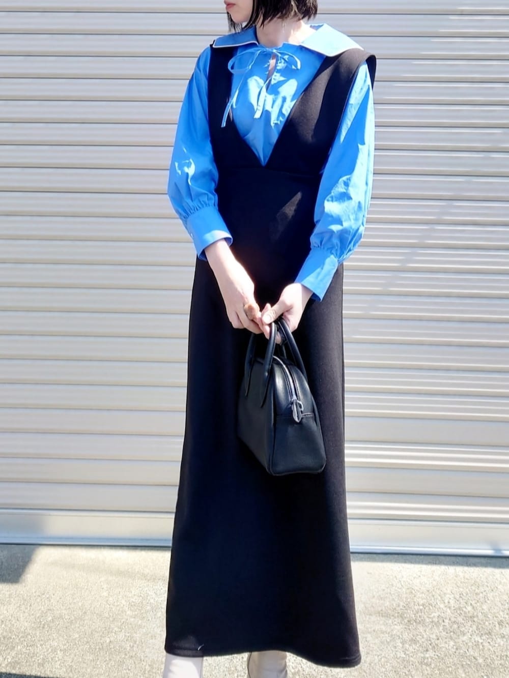 ブルー系のシャツ/ブラウス、ブラック系のジャンパースカート、ホワイト系のブーツを着用したレディースの春コーディネートの2枚目の写真