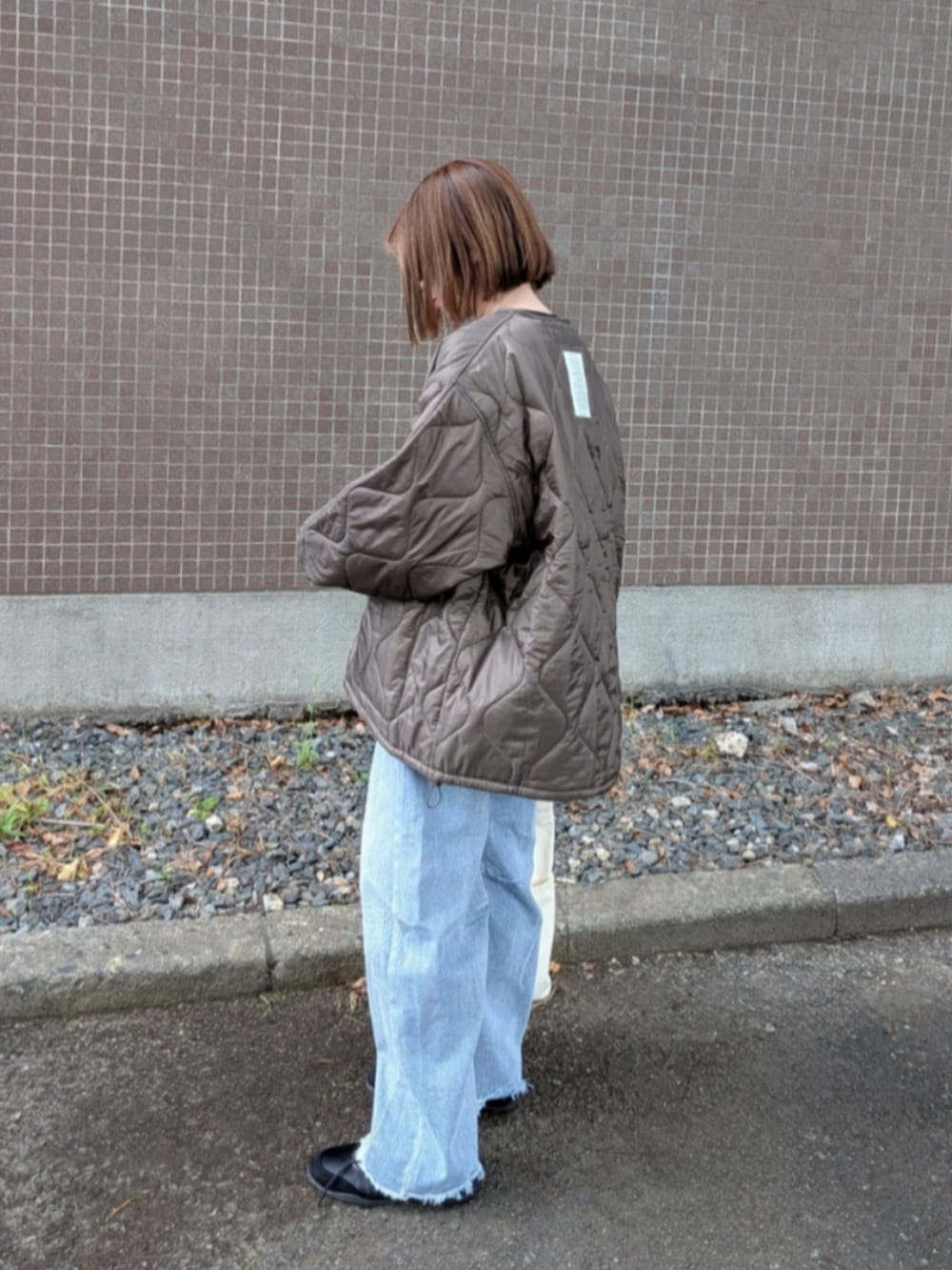 ブラウン系のブルゾン、ブルー系のデニムパンツ、ホワイト系のトートバッグを着用したレディースの秋コーディネートの2枚目の写真