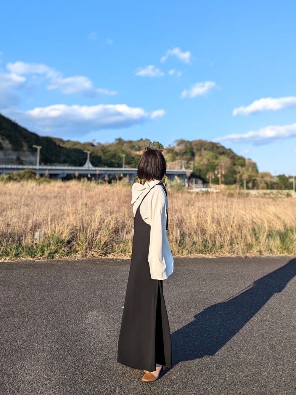 ブラック系のワンピース、ホワイト系のショルダーバッグ、ブラウン系のブーツを着用したレディースの春コーディネートの2枚目の写真