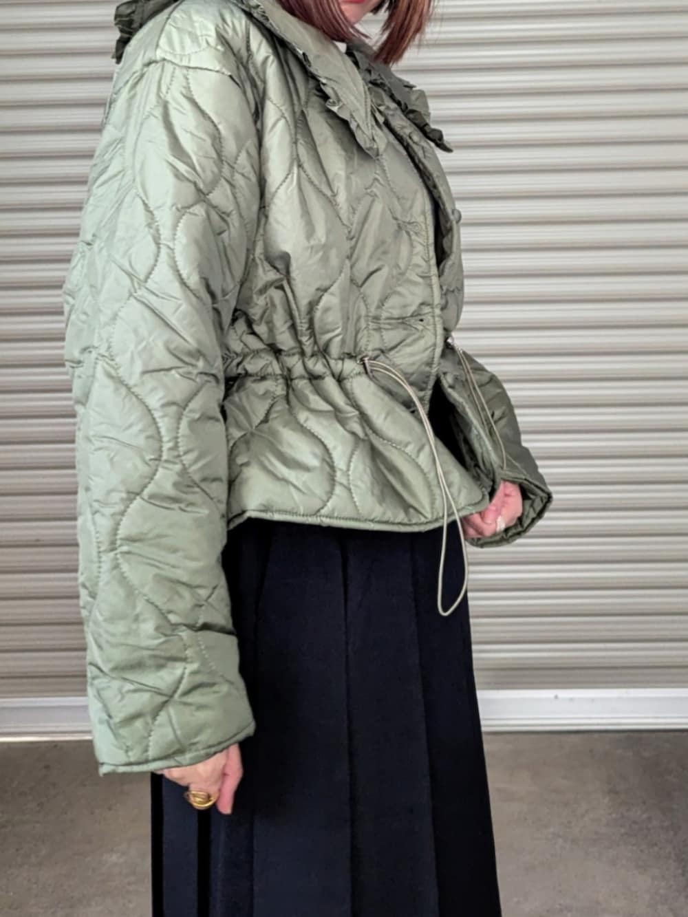 グリーン系のダウンジャケット/コート、ホワイト系のニット/セーター、ブラック系のブーツを着用したレディースの秋コーディネートの3枚目の写真