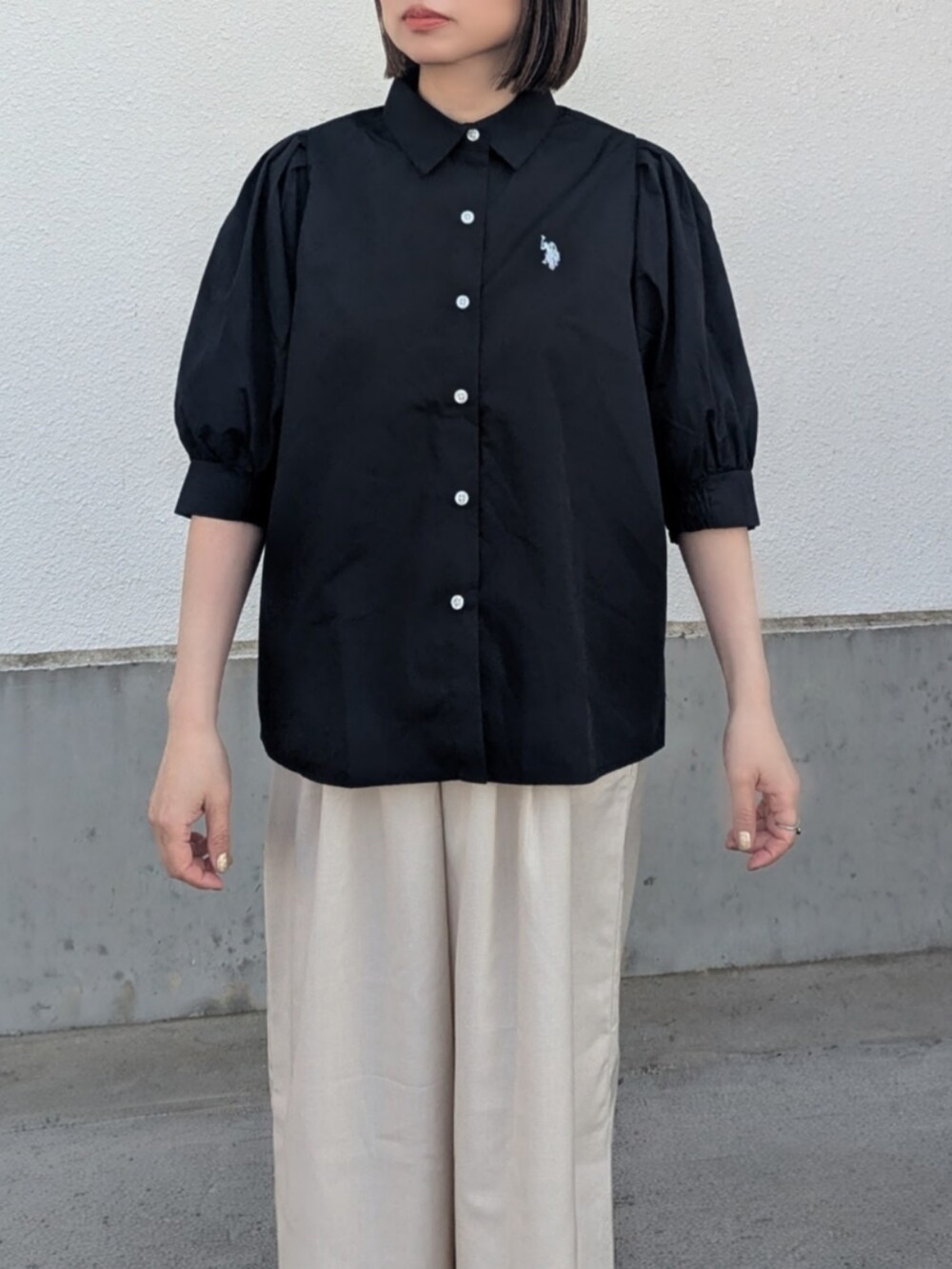 ブラック系のシャツ/ブラウス、ベージュ系のスラックス、ブラック系のパンプスを着用したレディースの春コーディネートの2枚目の写真