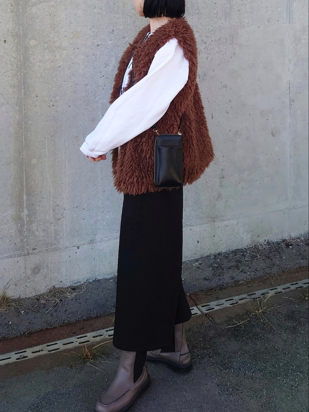 ホワイト系のスウェット、ブラウン系のベスト、ブラック系のボディバッグ/ウエストポーチを着用したレディースの冬コーディネートの3枚目の写真