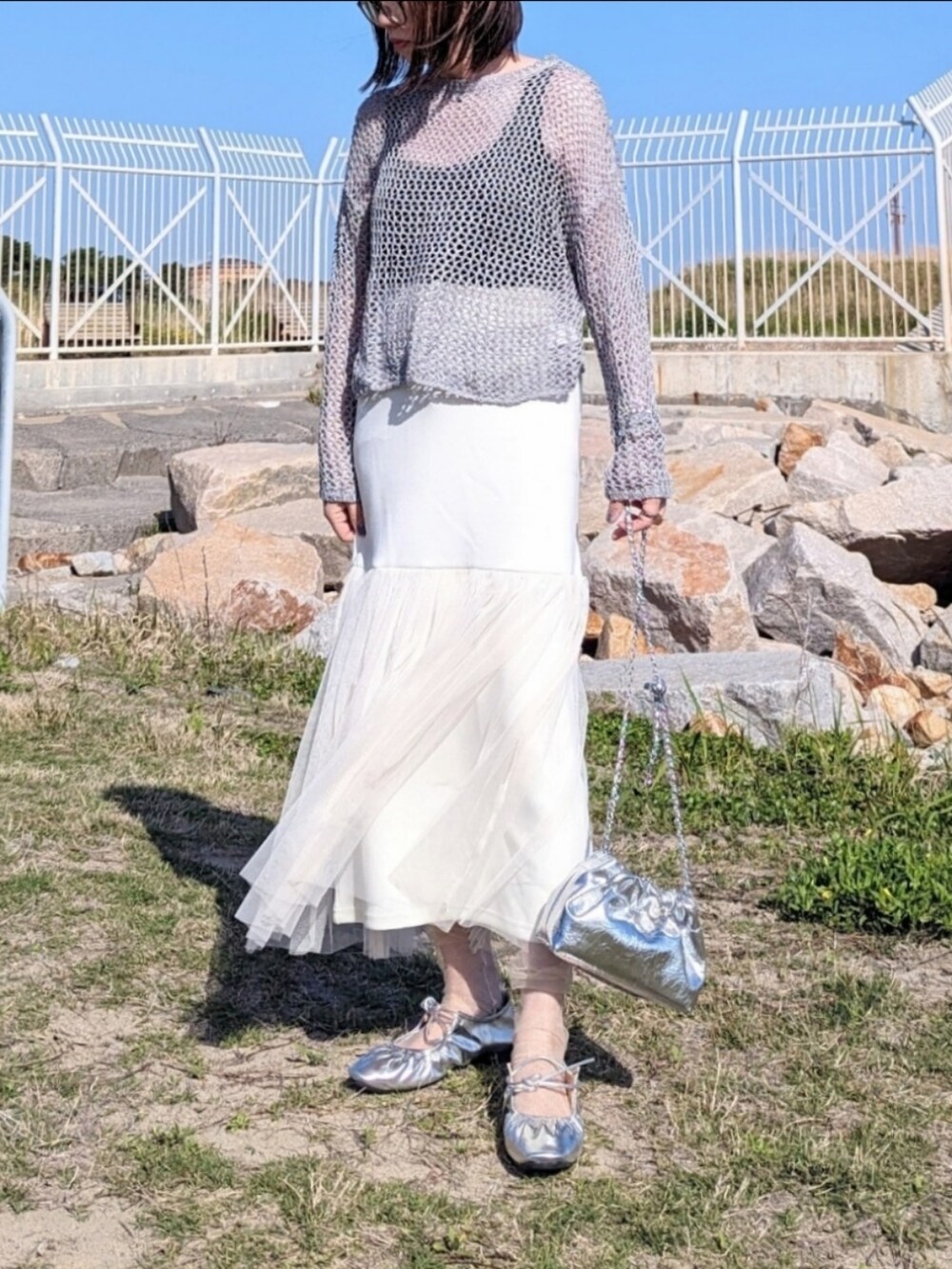 ホワイト系のスカート、グレー系のニット/セーター、シルバー系のショルダーバッグを着用したレディースの春コーディネートの2枚目の写真