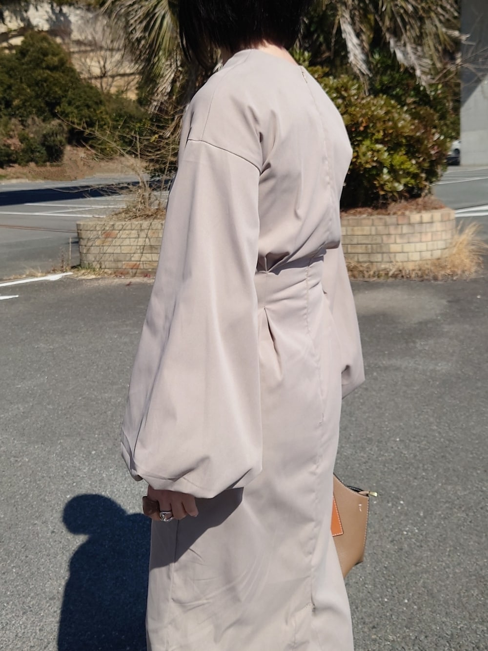 ベージュ系のワンピース、ホワイト系のブーツ、ブラウン系のハンドバッグを着用したレディースの春コーディネートの2枚目の写真