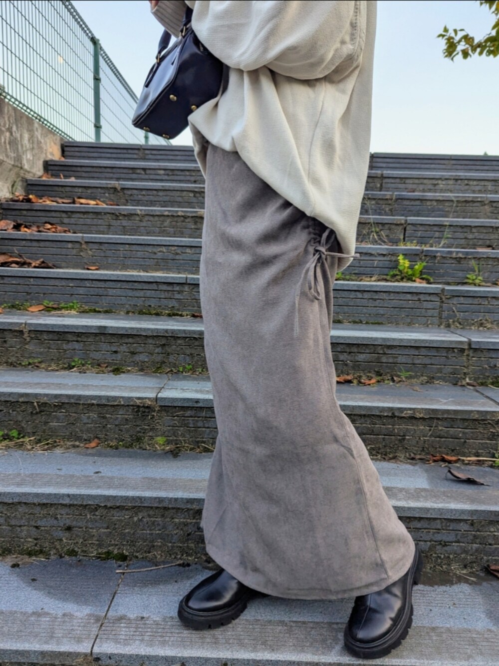 グレー系のスカート、ホワイト系のニット/セーター、ブラック系のブーツを着用したレディースの秋コーディネートの2枚目の写真