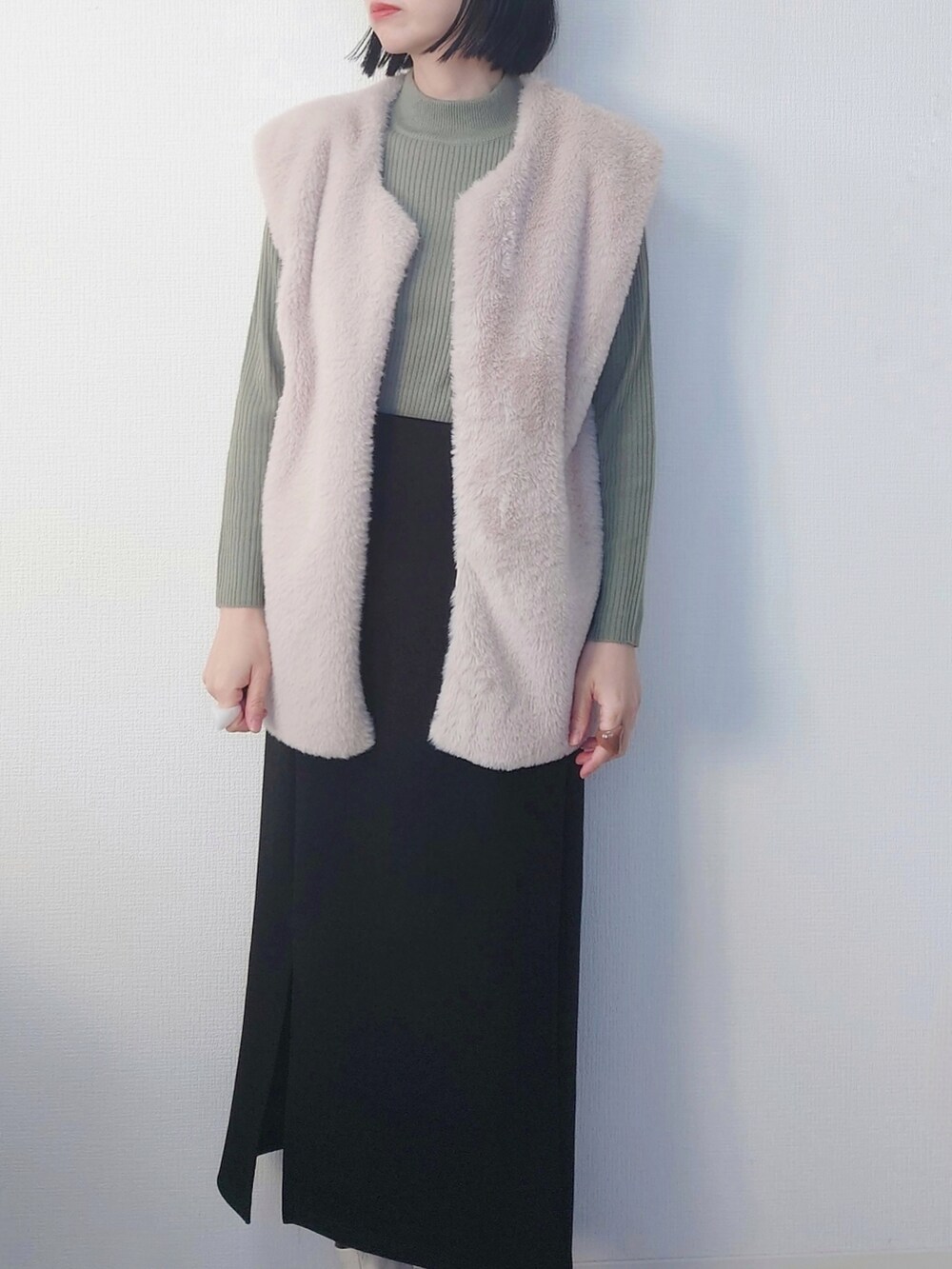 ブラック系のスカート、グリーン系のニット/セーター、ベージュ系のベストを着用したレディースの冬コーディネートの2枚目の写真