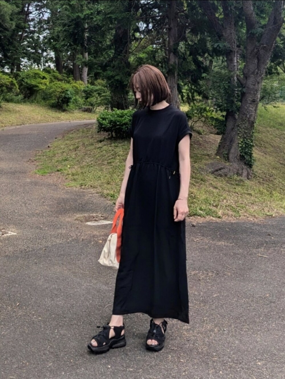 ブラック系のワンピース、オレンジ系のトートバッグ、ブラック系のサンダルを着用したレディースの夏コーディネートの2枚目の写真