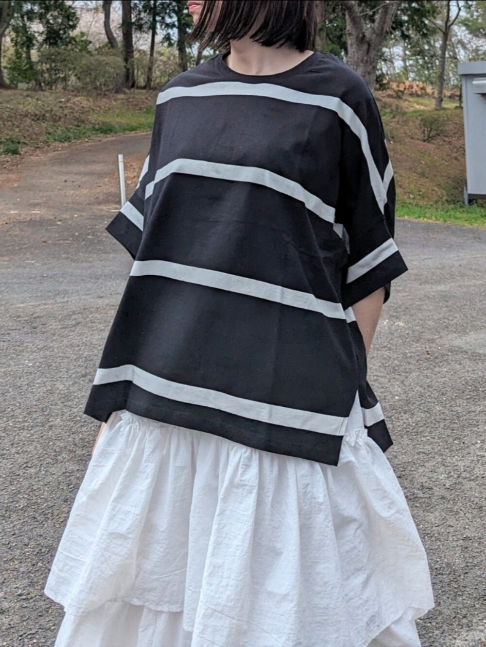 ブラック系のTシャツ/カットソー、ホワイト系のスカート、ベージュ系のスニーカーを着用したレディースの春コーディネートの2枚目の写真