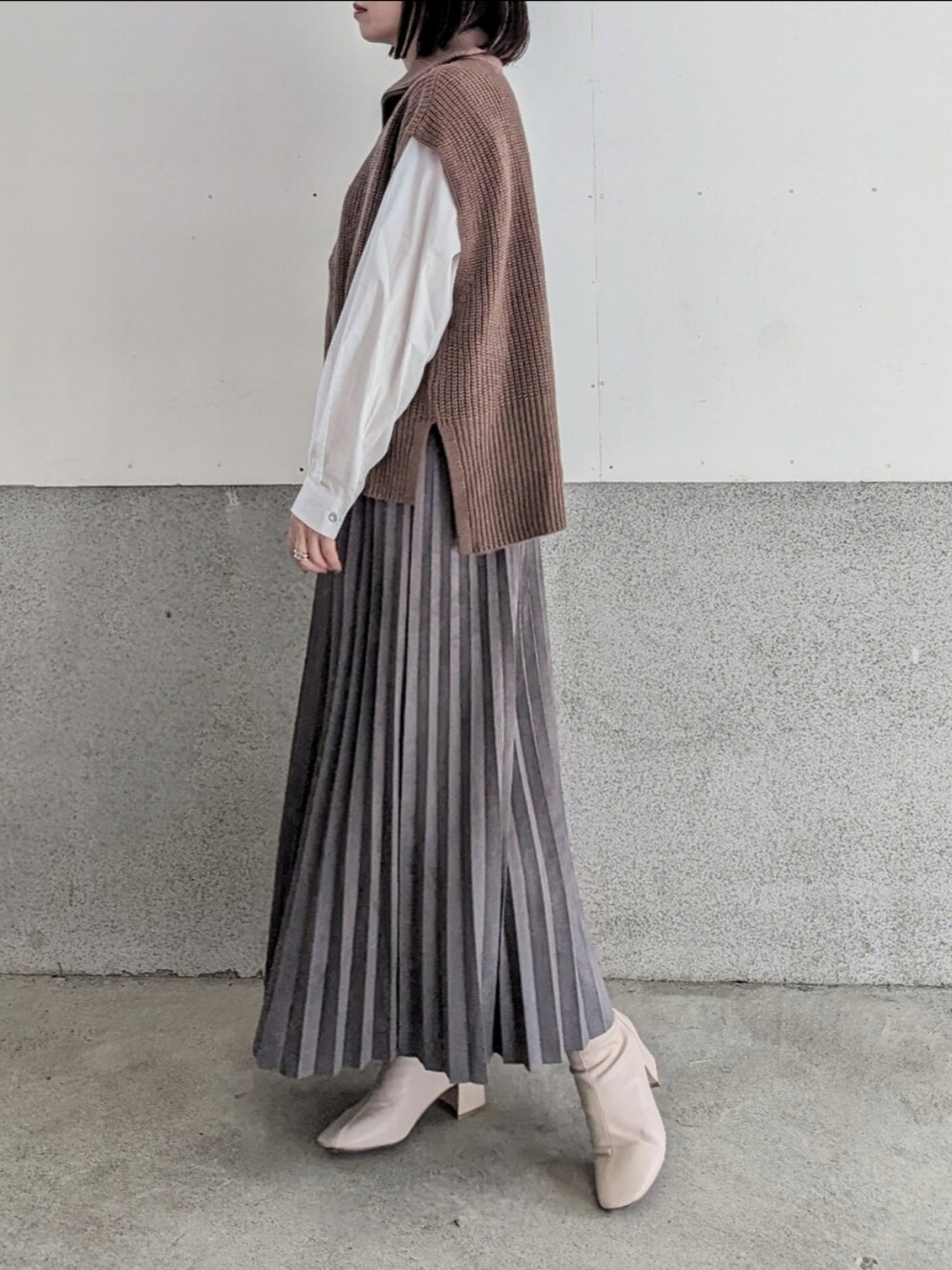 ブラウン系のベスト、グレー系のスカート、ホワイト系のハンドバッグを着用したレディースの秋コーディネートの2枚目の写真