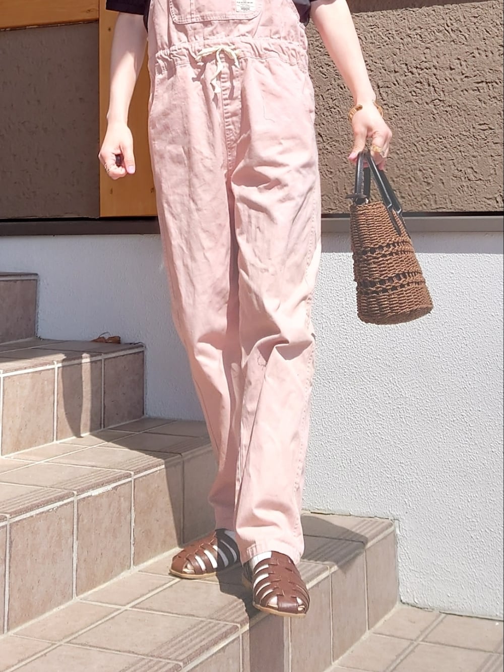 ブラウン系のハンドバッグ、ブラウン系のサンダル、ピンク系のオールインワン・サロペットを着用したレディースの春コーディネートの2枚目の写真