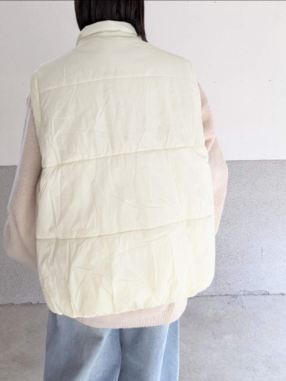 ベージュ系のニット/セーター、ホワイト系のダウンベスト、ブルー系のデニムパンツを着用したレディースの秋コーディネートの3枚目の写真