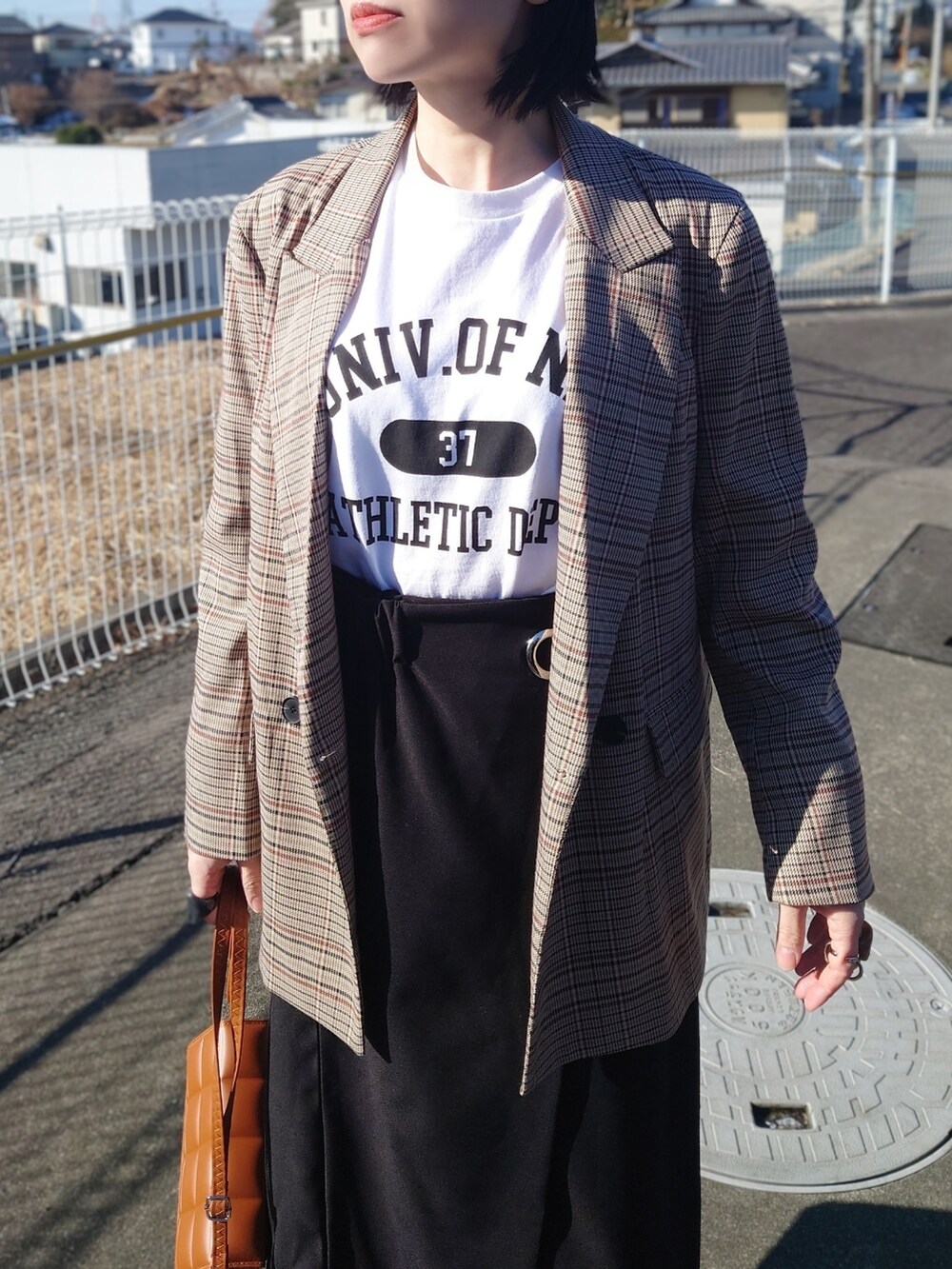 ホワイト系のTシャツ/カットソー、ブラック系のスカート、ブラウン系のクラッチバッグを着用したレディースの冬コーディネートの2枚目の写真