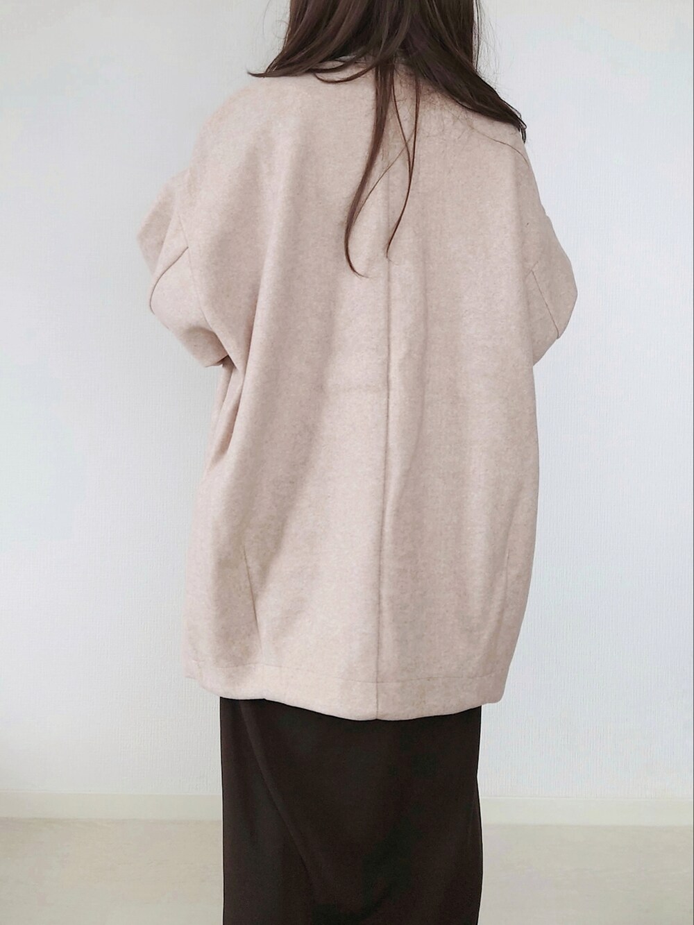 ベージュ系のノーカラーコート、ブラウン系のクラッチバッグ、ブラウン系のワンピースを着用したレディースの秋コーディネートの3枚目の写真