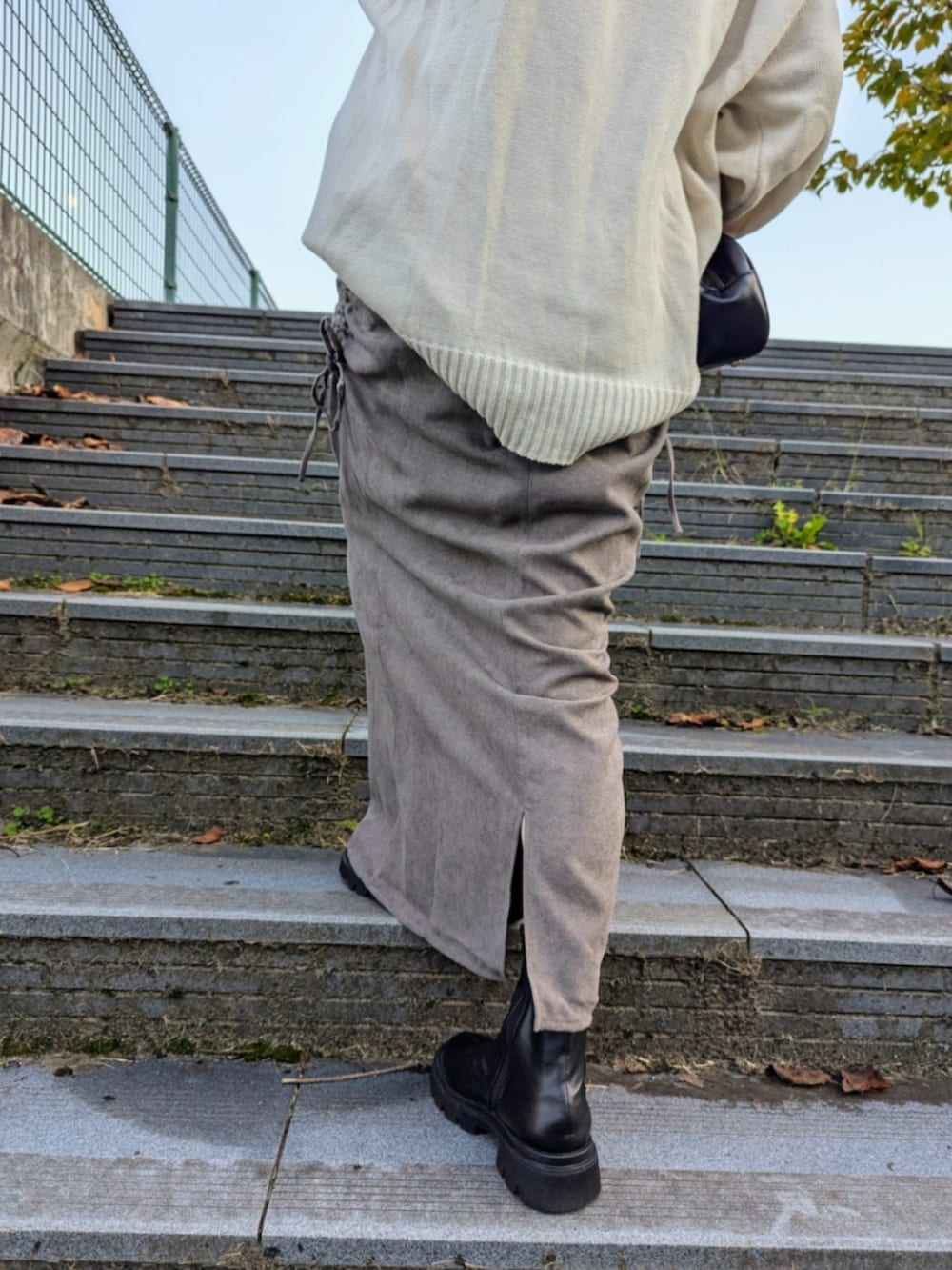 グレー系のスカート、ホワイト系のニット/セーター、ブラック系のブーツを着用したレディースの秋コーディネートの3枚目の写真