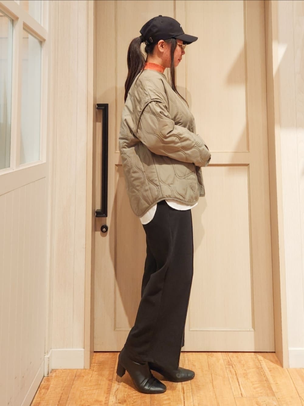 グリーン系のその他アウター、オレンジ系のニット/セーター、ブラック系のその他パンツを着用したレディースの冬コーディネートの2枚目の写真