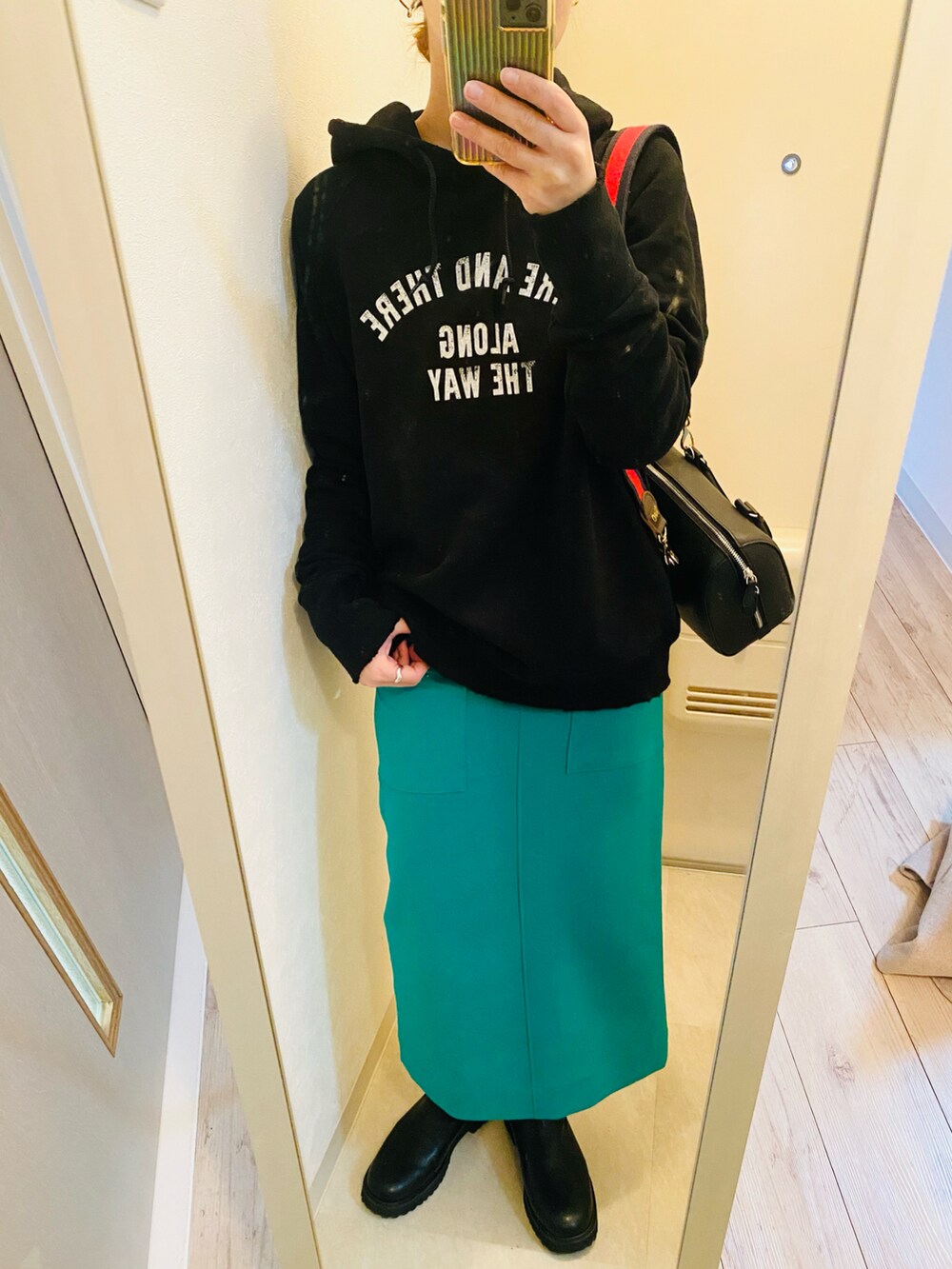 ブラック系のパーカー、グリーン系のスカート、ブラック系のブーツを着用したレディースの冬コーディネートの3枚目の写真