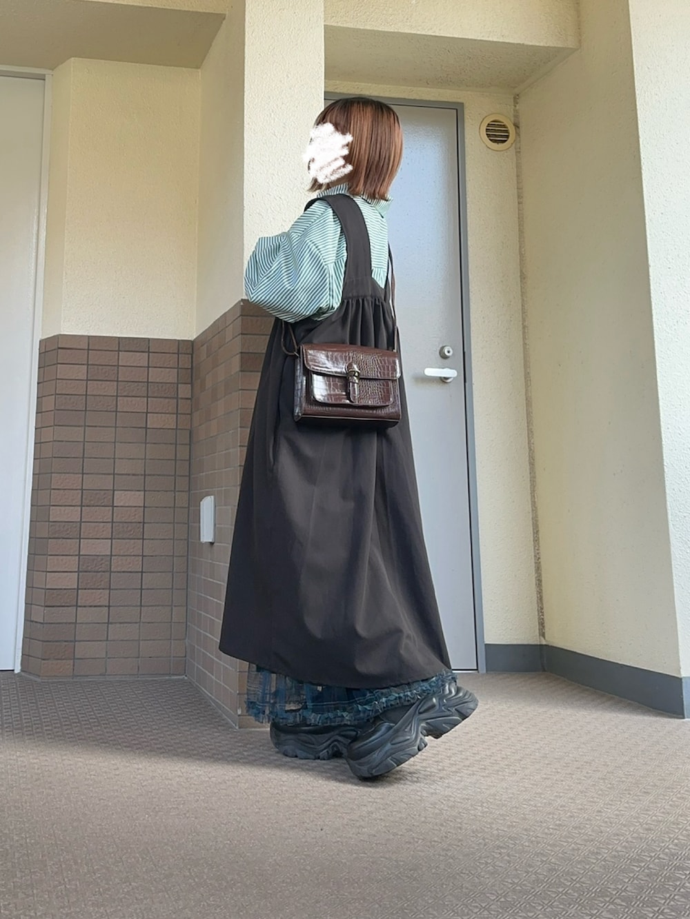 グリーン系のスカート、ブラック系のブーツ、グレー系のジャンパースカートを着用したレディースの春コーディネートの3枚目の写真