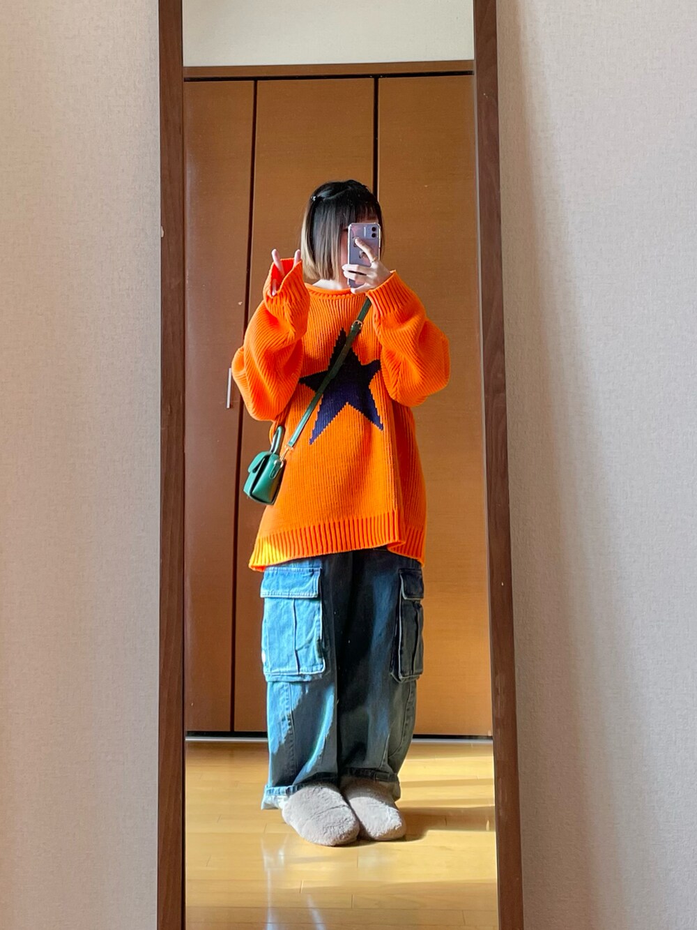 ブルー系のデニムパンツ、オレンジ系のニット/セーター、グリーン系のショルダーバッグを着用したレディースの春コーディネートの2枚目の写真