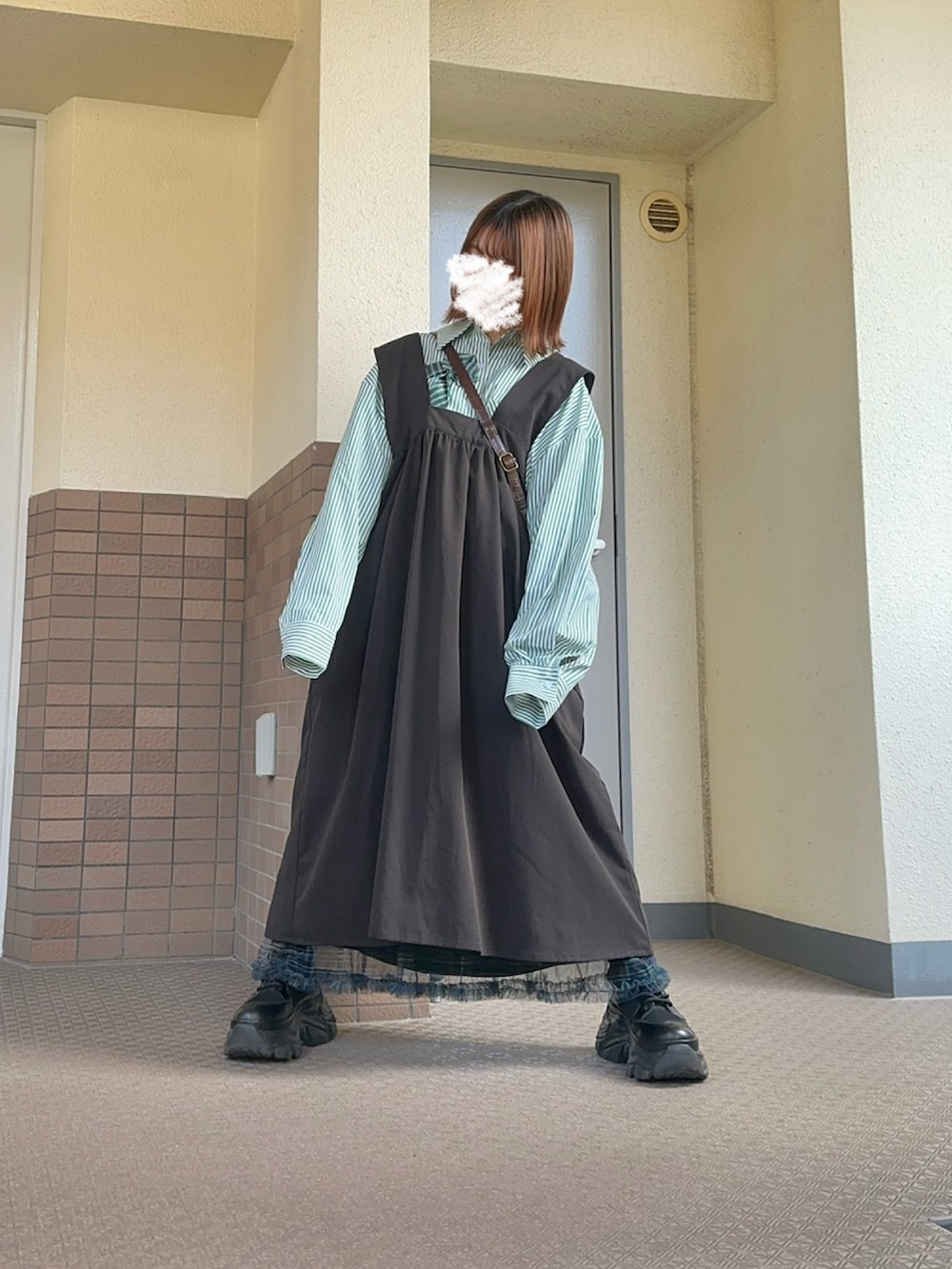 グリーン系のスカート、ブラック系のブーツ、グレー系のジャンパースカートを着用したレディースの春コーディネートの2枚目の写真