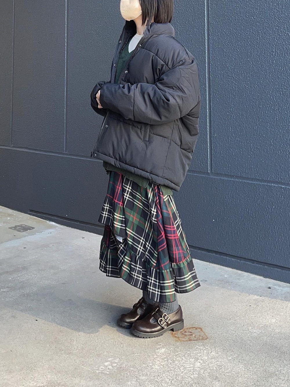 グリーン系のベスト、ブラック系のダウンジャケット/コート、グリーン系のスカートを着用したレディースの秋コーディネートの2枚目の写真