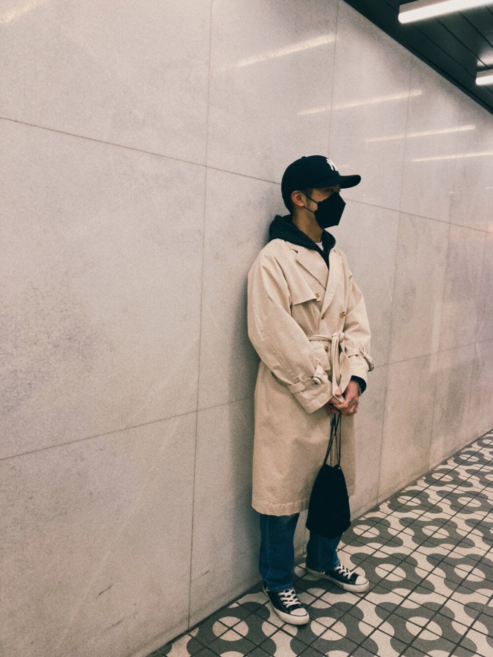 ベージュ系のトレンチコート、ブラック系のパーカー、ブラック系のハンドバッグを着用したメンズの春コーディネートの2枚目の写真