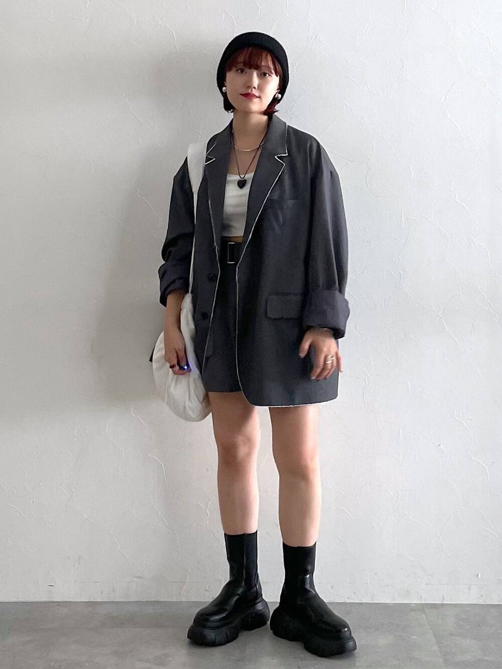 グレー系のテーラードジャケット、ブラック系のブーツ、ホワイト系のショルダーバッグを着用したレディースの秋コーディネートの2枚目の写真