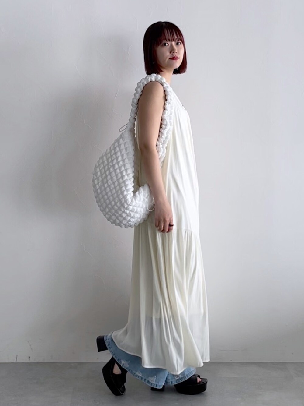 ホワイト系のワンピース、ホワイト系のショルダーバッグ、ブルー系のデニムパンツを着用したレディースの春コーディネートの3枚目の写真