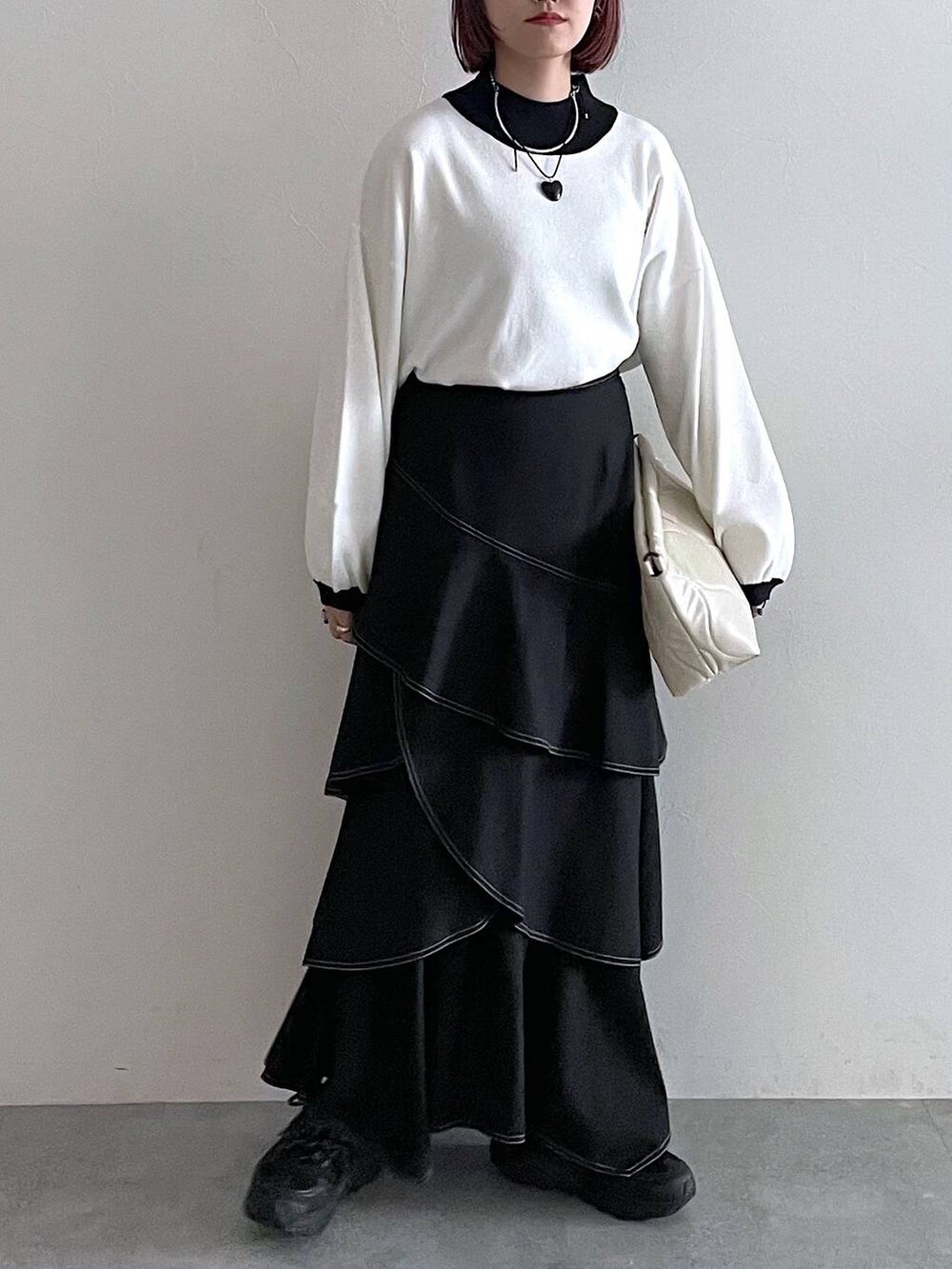 ホワイト系のニット/セーター、ホワイト系のクラッチバッグ、ブラック系のスカートを着用したレディースの秋コーディネートの3枚目の写真