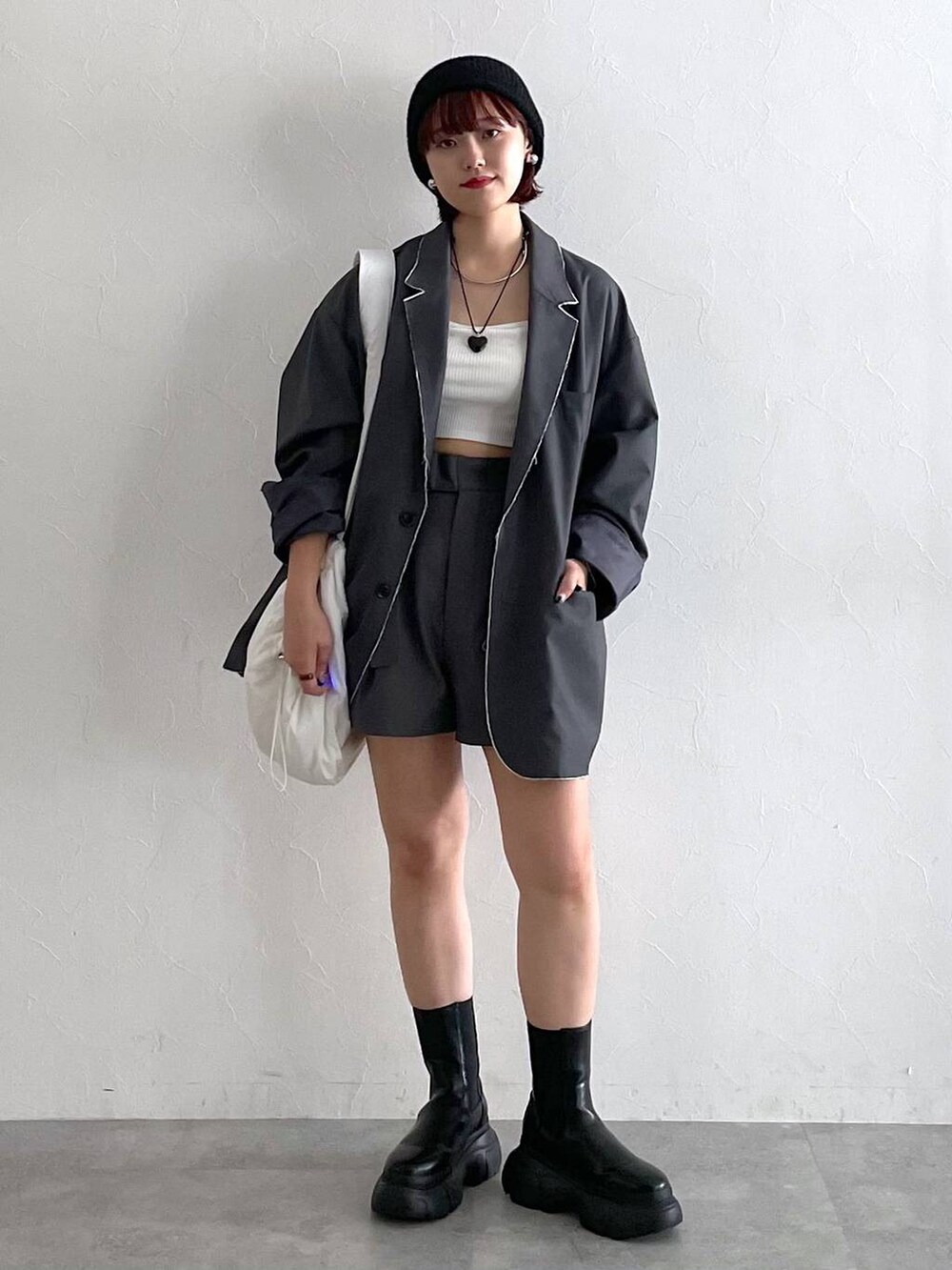 グレー系のテーラードジャケット、ブラック系のブーツ、ホワイト系のショルダーバッグを着用したレディースの秋コーディネートの4枚目の写真