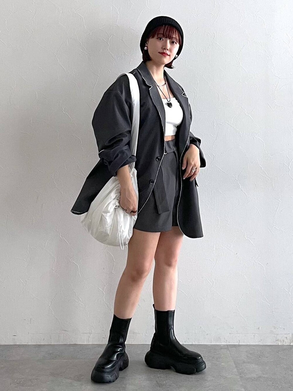 グレー系のテーラードジャケット、ブラック系のブーツ、ホワイト系のショルダーバッグを着用したレディースの秋コーディネートの3枚目の写真
