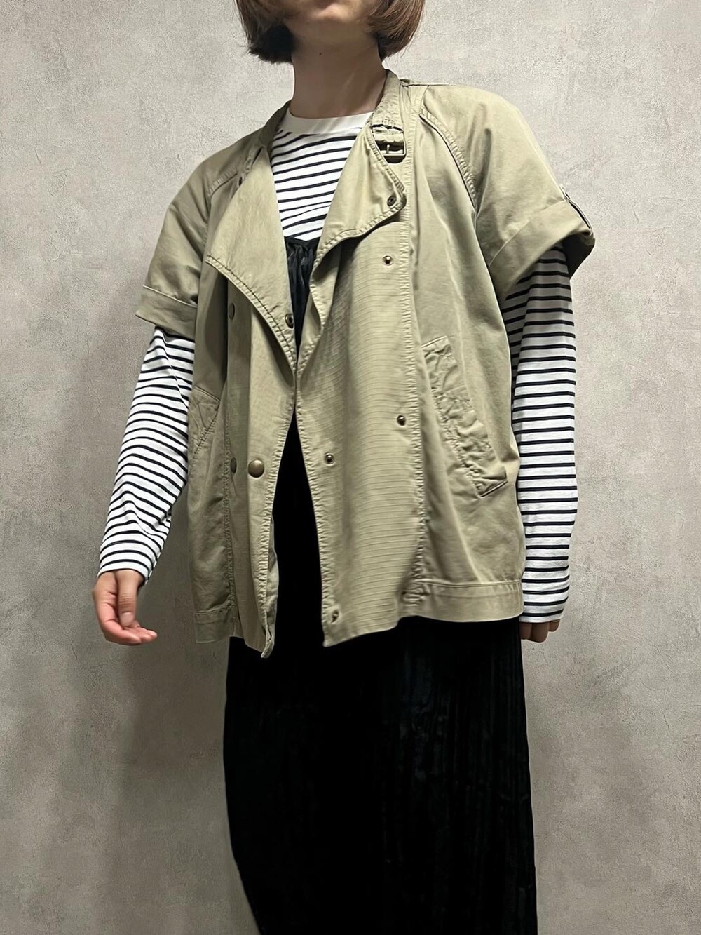 ベージュ系のミリタリージャケット、ブラック系のワンピースを着用したレディースの春コーディネートの2枚目の写真