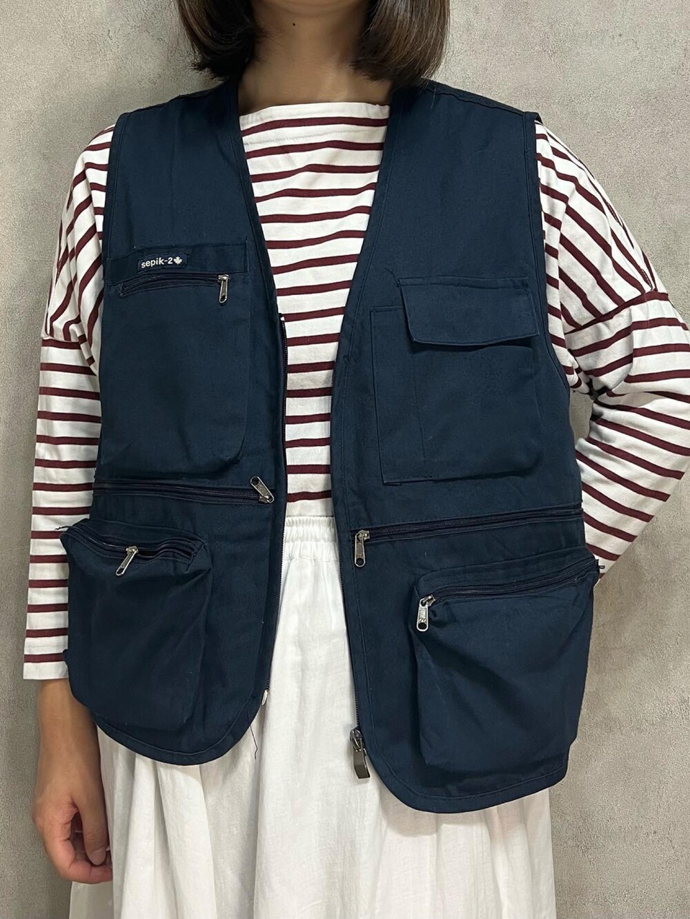 ホワイト系のスカート、ブルー系のベストを着用したレディースの秋コーディネートの2枚目の写真