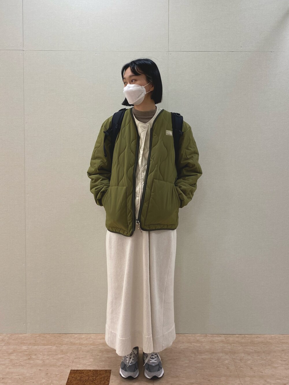 シルバー系のスニーカー、ベージュ系のダウンベスト、ホワイト系のワンピースを着用したレディースの冬コーディネートの2枚目の写真