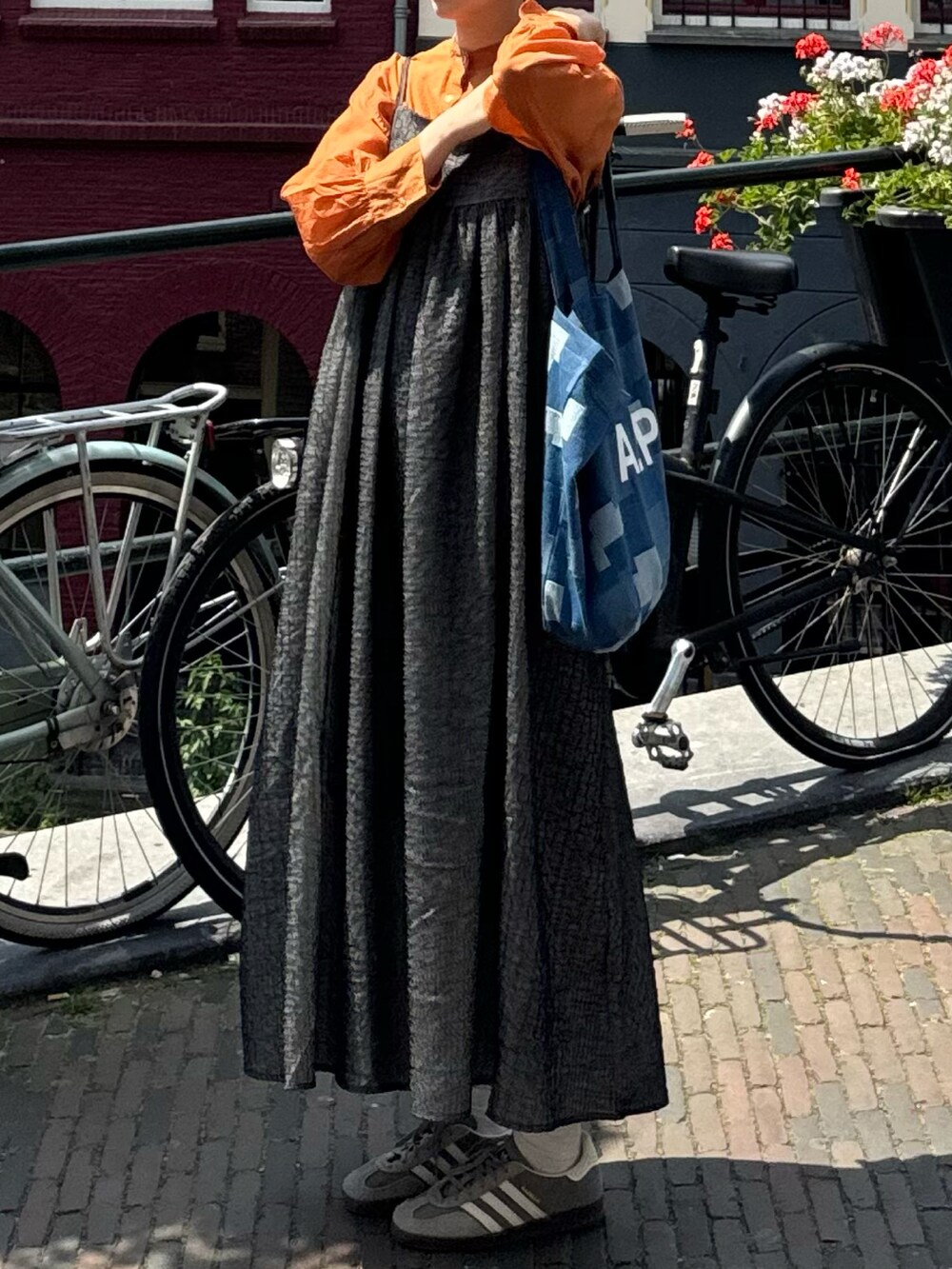 オレンジ系のシャツ/ブラウス、ブラック系のワンピース/ドレス、グレー系のシューズを着用したレディースの夏コーディネートの2枚目の写真