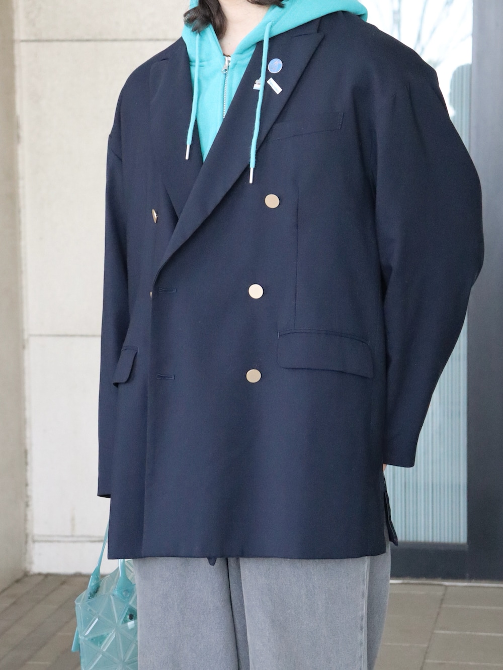 グリーン系のトートバッグ、ブルー系のテーラードジャケット、ブルー系のパーカーを着用したメンズの春コーディネートの4枚目の写真