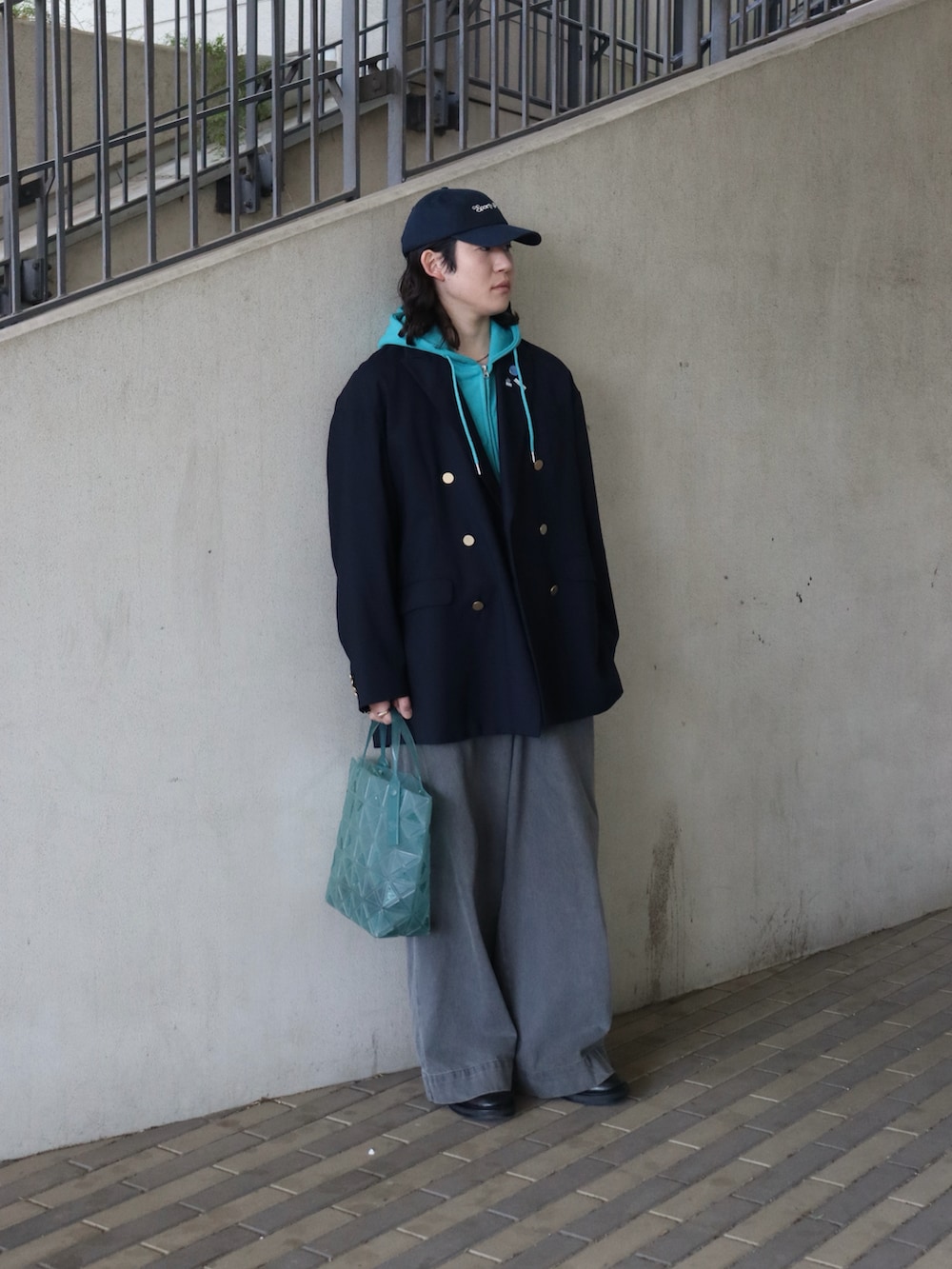グリーン系のトートバッグ、ブルー系のテーラードジャケット、ブルー系のパーカーを着用したメンズの春コーディネートの3枚目の写真