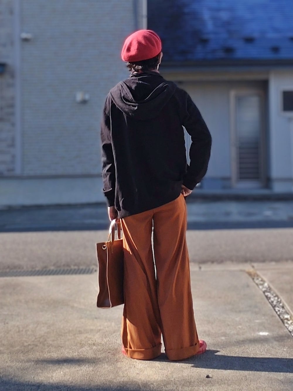 ブラック系のパーカー、オレンジ系のスラックス、ブラウン系のトートバッグを着用したメンズの秋コーディネートの2枚目の写真