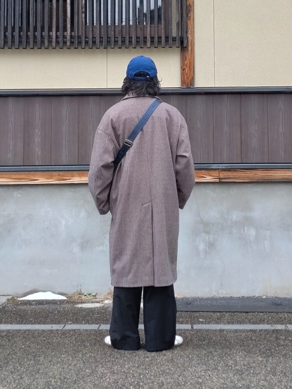 ブラウン系のステンカラーコート、ブルー系のショルダーバッグ、ブラック系のスラックスを着用したメンズの冬コーディネートの2枚目の写真