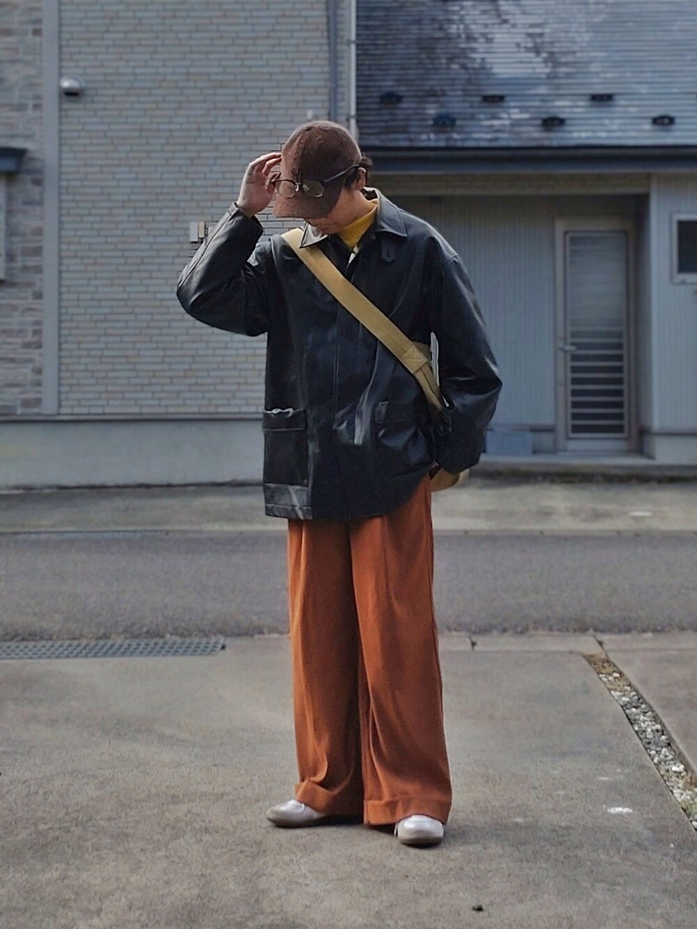 ブラック系のカバーオール、オレンジ系のスラックス、ブラウン系のキャップを着用したメンズの冬コーディネートの2枚目の写真